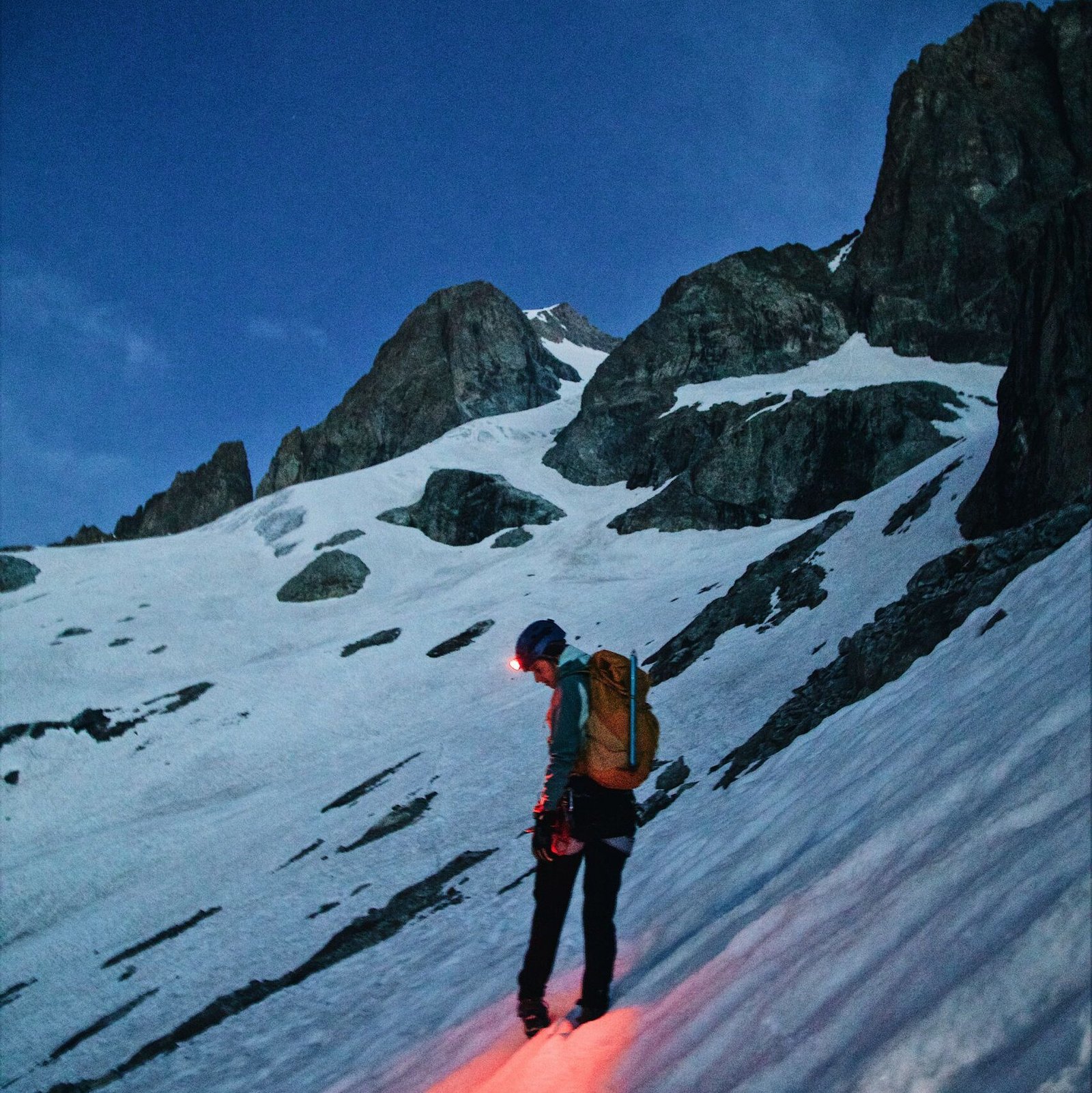 A lone climber explores a snowy mountain under a starry night sky, showcasing adventure.